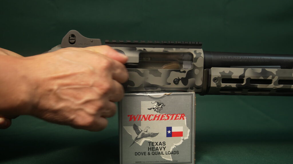 Hand running the bolt of a gray camo Benelli M4 TRIARC build